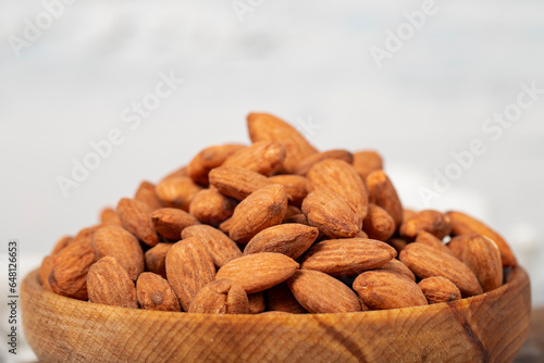 Almond in wood bowl. Roasted almonds on white wood background. Close up