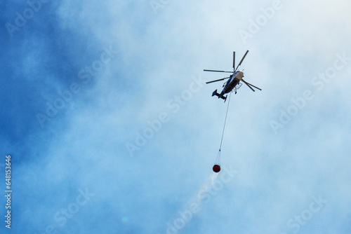 tragic view of forest fire and helibucket which is a specialized bucket suspended on a cable carried by a helicopter to deliver water for aerial firefighting 