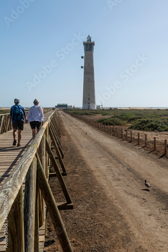 A couple walks hand in hand towards the beach where the lighthouse is located, Matorral, Fuerteventura, Canary Islands, Spain
