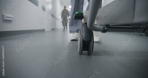 Doctor, nurse or paramedic move gurney with seriously injured patient towards surgery room. Medic save human life. Medical staff legs close up. Bright medical facility corridor. Emergency department.