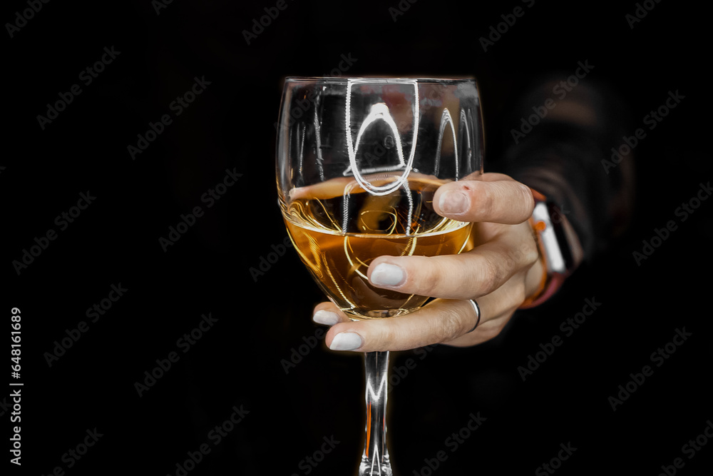 A woman's hand holds out or holds a glass of alcoholic beverage from the darkness close up A woman's hand holds out or holds a glass of alcoholic beverage from the darkness close up