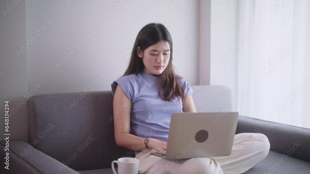 Pretty Asian woman surfing social media or working on laptop while lying on the sofa when relax in living room at home., Concept of activity in living room. Pretty Asian woman surfing social media or working on laptop while lying on the sofa when relax in living room at home., Concept of activity in living room.