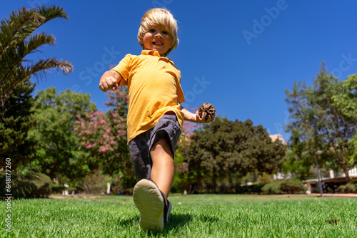 a little blond boy of three years old runs in the park on the green grass