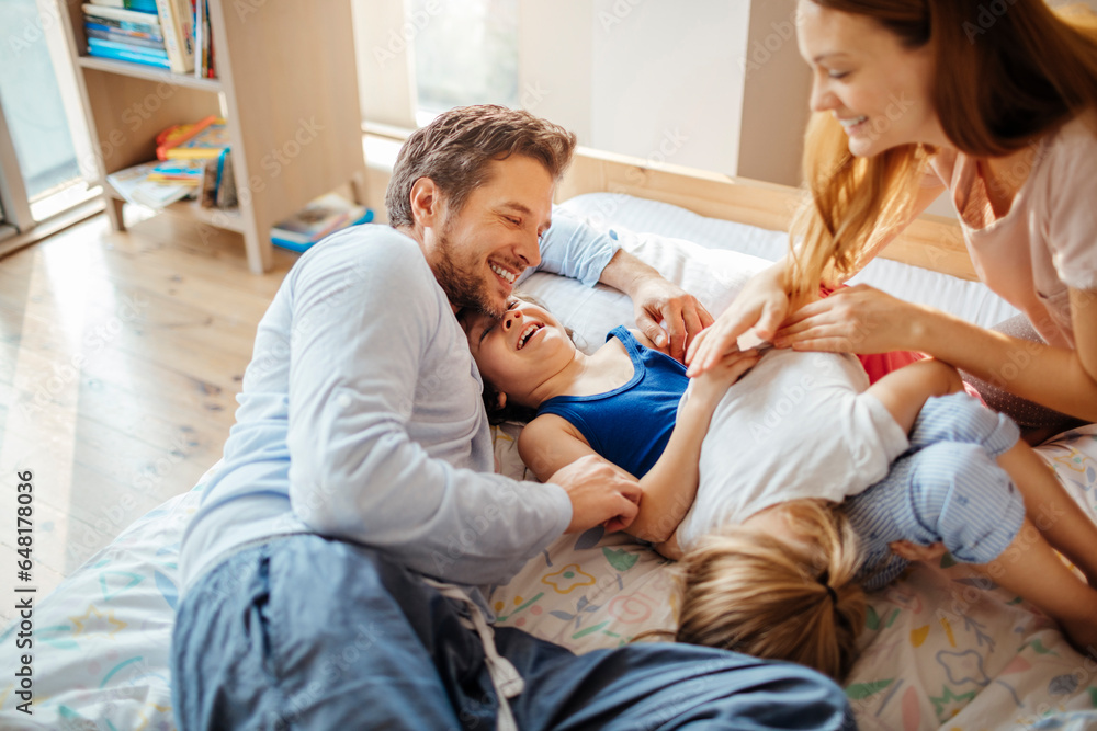 Young Caucasian family having fun and playing together in the bedroom in their pajamas