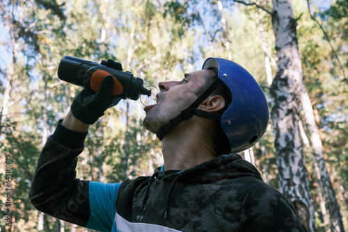 traveler in a protective helmet and gloves stopped in the forest and drinks water from a bottle.Active lifestyle