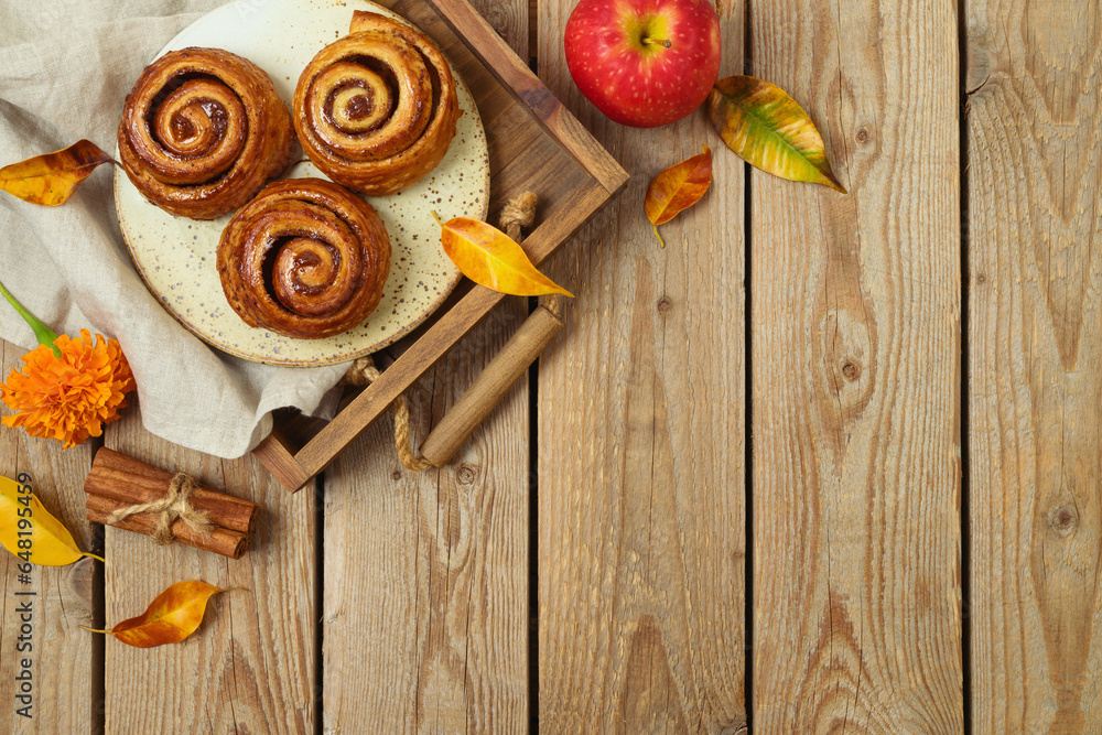 Autumn concept with freshly baked cinnamon buns and fall leaves on wooden background. Top view, flat lay Autumn concept with freshly baked cinnamon buns and fall leaves on wooden background. Top view, flat lay