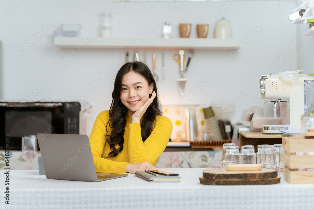 Beautiful Asian woman smiling happily relaxing using technology of laptop computer Take notes Drink a relaxing hot drink while sitting on the table in your room at home. Beautiful Asian woman smiling happily relaxing using technology of laptop computer Take notes Drink a relaxing hot drink while sitting on the table in your room at home.