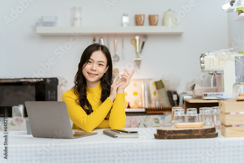 Beautiful Asian woman smiling happily relaxing using technology of laptop computer Take notes Drink a relaxing hot drink while sitting on the table in your room at home. © Kritdanai