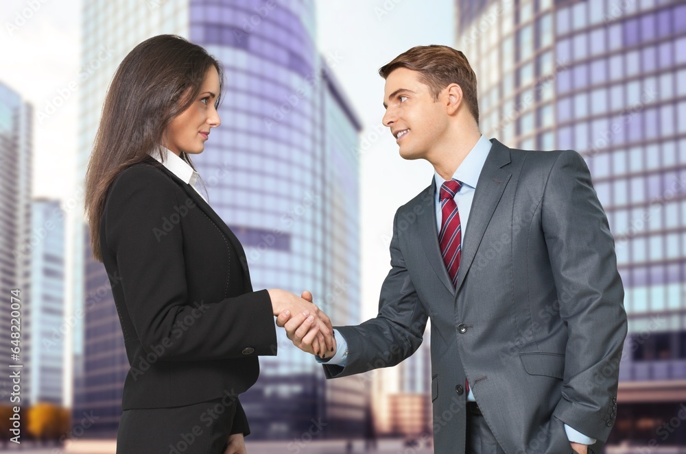 Business partners shaking hands on office building background Business partners shaking hands on office building background