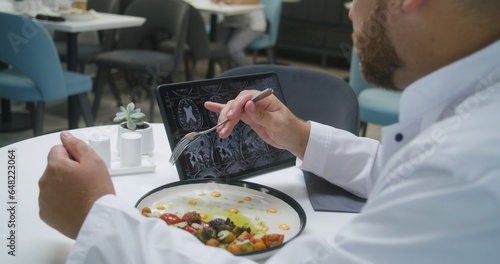 Professional doctor watches image of MRI or CT scan using digital tablet in clinic cafe. Medic eats his dinner  examines brain scanning results of patient. Medical staff have meal in hospital canteen.