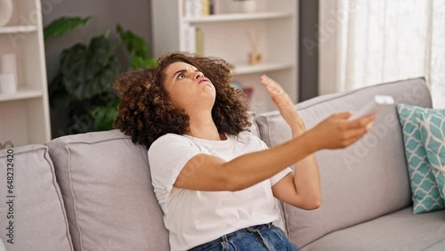 Young beautiful hispanic woman suffering for hot using book as a hand fan at home