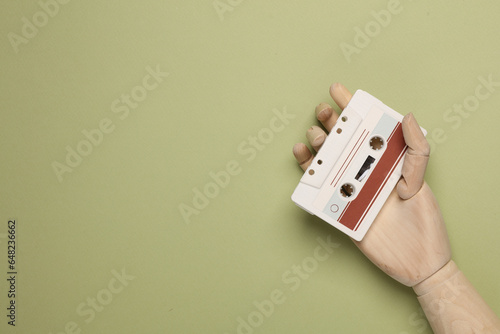 Wooden hand holding retro 80s audio cassette on green background