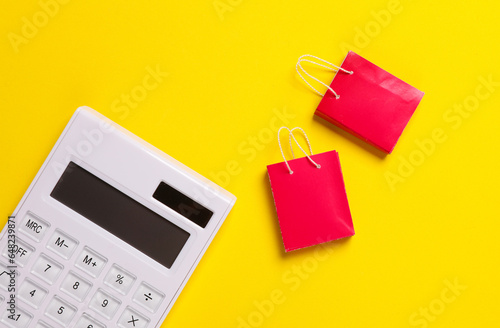 Calculator with miniature shopping bags on a yellow background. Sale concept