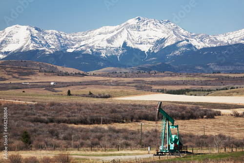 Pumpjack in the foothills with snow covered mountains and blue sky; Longview Alberta Canada photo