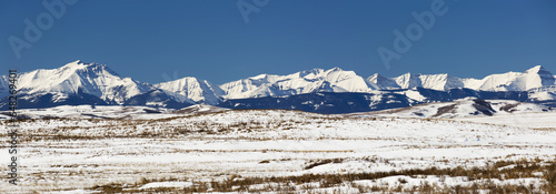 Panarama Of Snow Covered Rolling Hills With Snow Covered Mountains In The Background With Blue Sky; Longview, Alberta, Canada photo