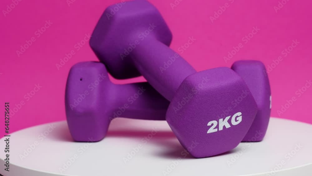 Two rubberized dumbbells of 2 kg of purple color rotate on a pink background. Preparation for sports training. Two rubberized dumbbells of 2 kg of purple color rotate on a pink background. Preparation for sports training.