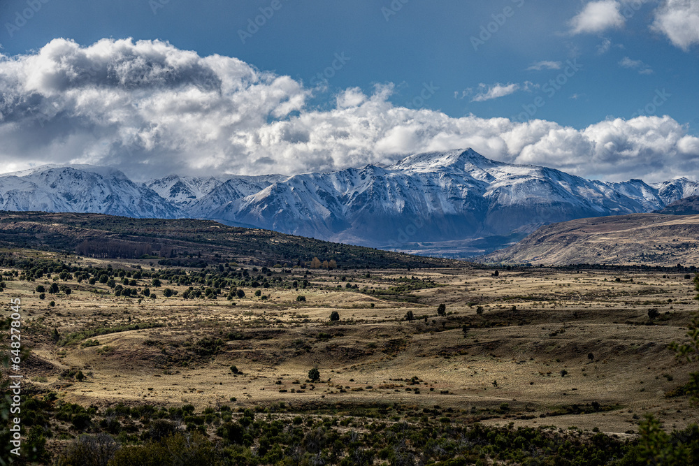 Landscape in Los Alerces National Park, Chubut, Argentina. A mountain range in warm tones with a background of cold blue Andes mountains covered in snow.