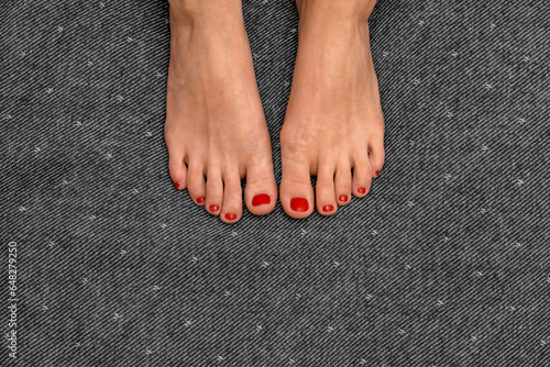 When passion passes through the foot. Feet of a young girl with fiery red nail polish on gray and white uniform textured background. Neutral space and focus on beautiful well-groomed female legs.