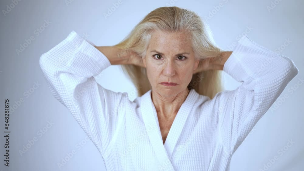 Slow motion portrait of middle-aged caucasian old mature woman in bathrobe putting fingers through hair. Beautiful senior lady spa self care beauty routine natural shampoo conditioner
