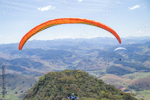 A person flying in a parachute in front of mountain with lots of trees.