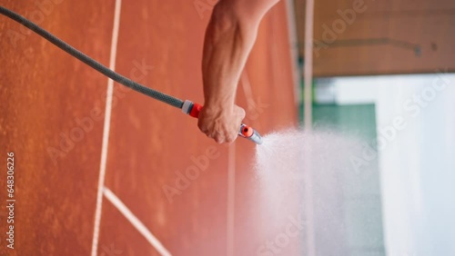 vertical video close-up hand holds a hose and waters the ground outdoor tennis court with water prepares the location for competitions and training photo