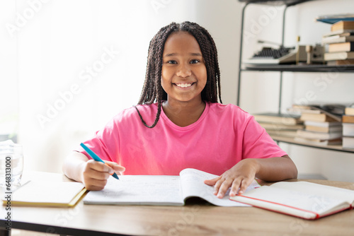 Portrait attractive African American girl wearing stylish pink t-shirt sitting at table, holding pen