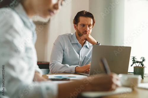 Two coworkers working together on project while using laptop in office meeting room