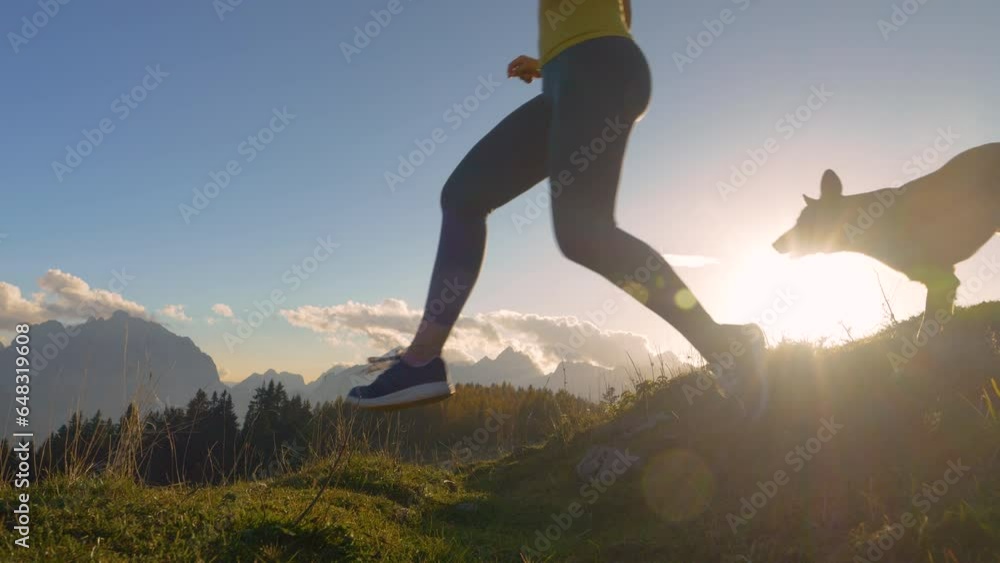 Running Environments CLOSE UP, LENS FLARE: Agile young lady runs down the grassy hill with ...