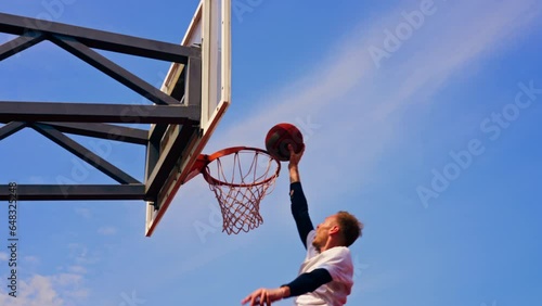 Tall guy basketball player jumps to the hoop with the ball in his hand to score a spectacular dunk during practice on the basketball court in the park