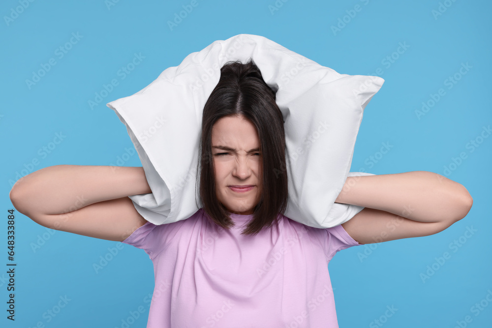 Irritated young woman covering ears with pillow on light blue background. Insomnia problem Irritated young woman covering ears with pillow on light blue background. Insomnia problem