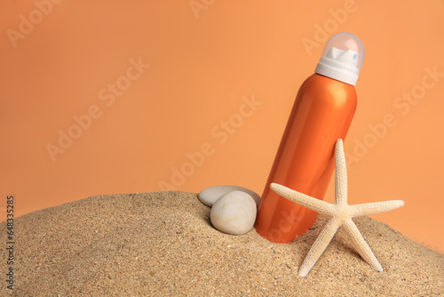 Sand with bottle of sunscreen, starfish and stones against orange background, space for text. Sun protection