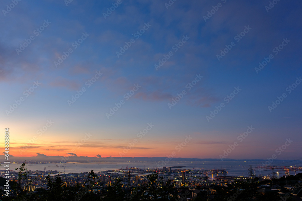 夜明け前のオレンジ色に染まる空と湾岸。神戸市の高台から大阪湾と大阪南港をのぞむ。