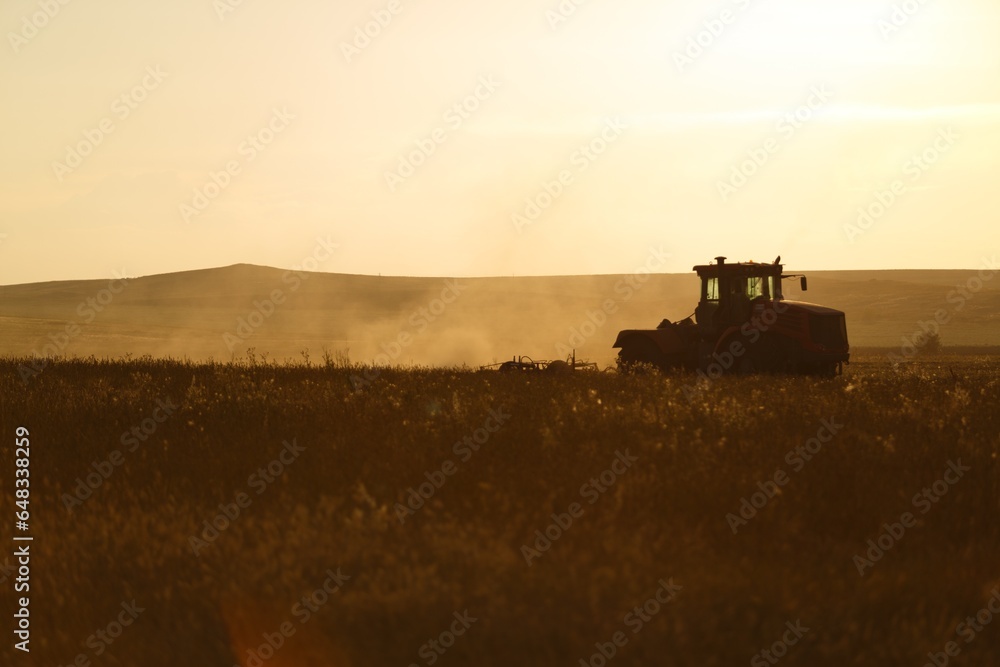 Fototapeta premium Tractor working on the field in the sunset light