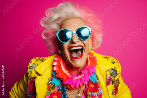 A jubilant senior woman, dressed in a colorful neon outfit, dons quirky sunglasses and showcases her extravagant style while sharing laughter and smiles in a trendy studio photoshoot.
