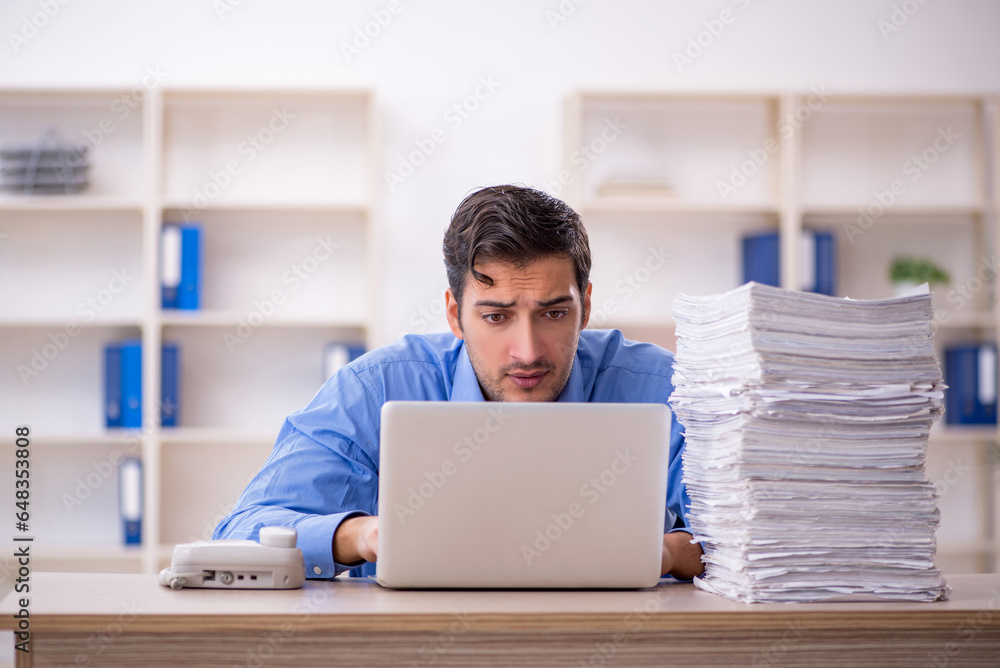 Young male employee and too much work in the office Young male employee and too much work in the office