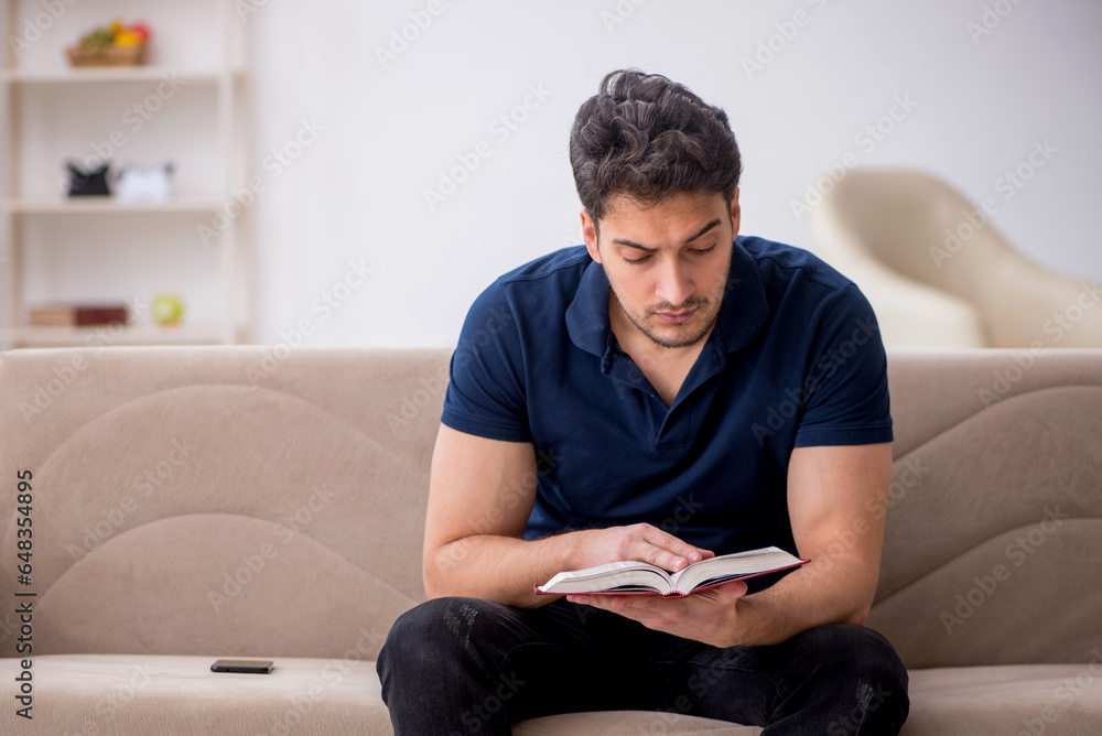 Young male student reading book at home