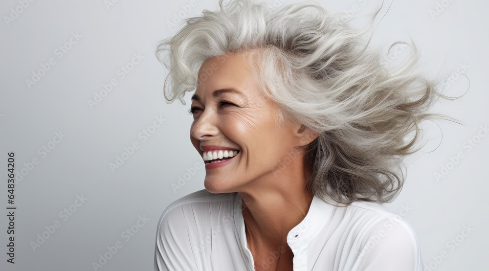 an old woman with short hair smiling in front of a gray background, timeless beauty