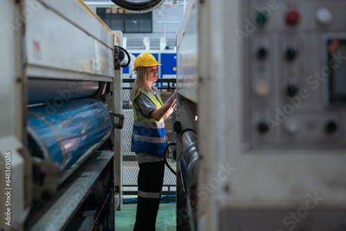 Male and female technicians are inspecting a large paper production machine.