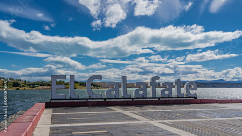 On the city embankment, the name of the city of El Calafate is set in large letters. Behind is the turquoise lake  Lago Argentino. Clouds in the blue sky. Argentina. photo