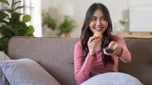 Women eating bread while watching tv and switching channel with remote control in lifestyle at home