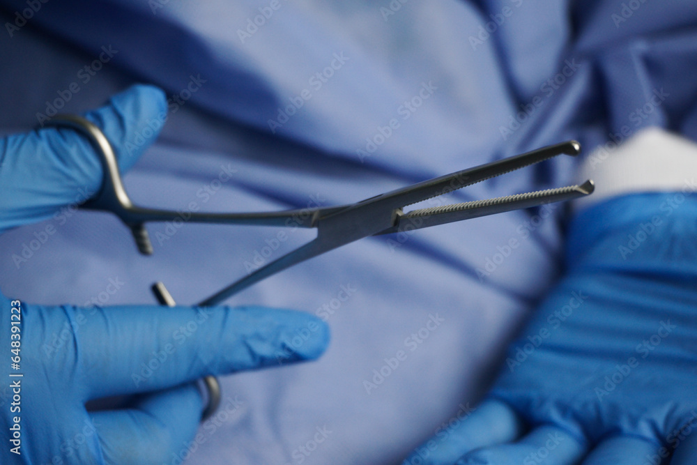 Doctor wearing blue medical gloves holding Allis Intestinal and Tissue