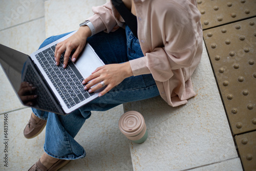 top view of laptop keyboard and woman's hands on the street, takeaway coffee mug
