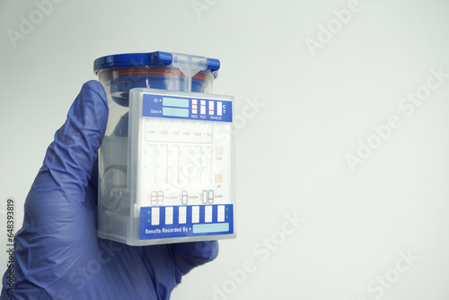 Hand in blue glove holding an empty container for analysis. Drug test concept. Isolated on white background.