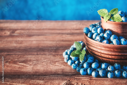 Blueberry harvest in clay bowls with mint leaves on a wooden background. Sunlight. Dark rustic style. Place for text.