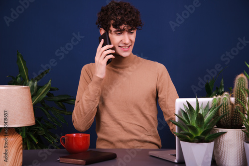 Funny curly guy working at a laptop. Blue background.