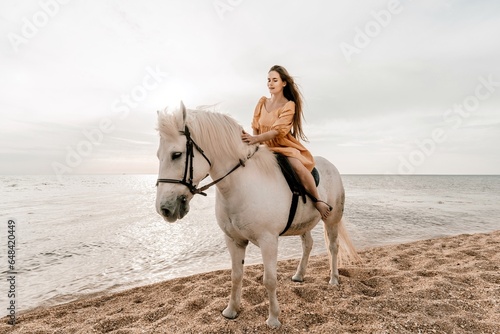 A white horse and a woman in a dress stand on a beach, with the sky and sea creating a picturesque backdrop for the scene.