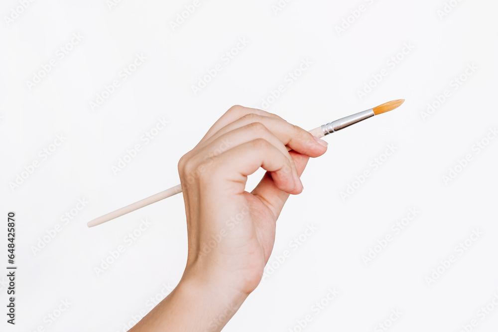 A female hand holding a paintbrush isolated on a white background. Mockup with empty copy space for text and design A female hand holding a paintbrush isolated on a white background. Mockup with empty copy space for text and design
