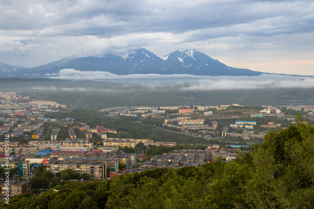 Beautiful landscape. Top view of residential urban areas. Volcanoes in the distance. Overcast weather. Low clouds. Summer cityscape. Petropavlovsk-Kamchatsky city, Kamchatka Krai, Far East of Russia.