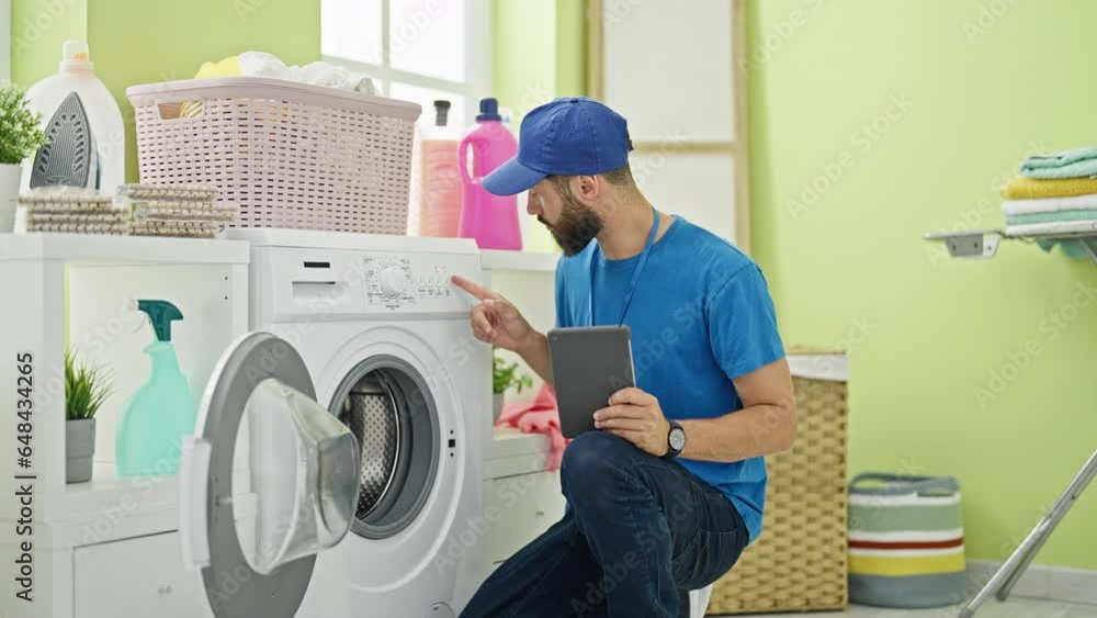 Young hispanic man technician repairing washing machine holding touchpad at laundry room Young hispanic man technician repairing washing machine holding touchpad at laundry room