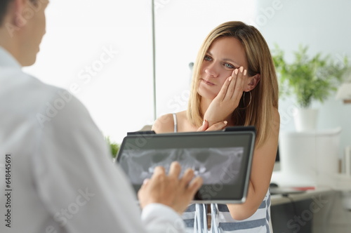 Fotografie Female patient with acute toothache at doctor appointment with X-ray image